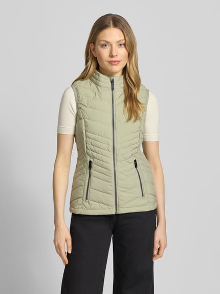 Frauenmodel trägt Steppweste mit 10.000 mm Wassersäule Modell 'GS109' von G.I.G.A. DX, Slim Fit, Stehkragen, Reißverschlusstaschen, helles Beige, glatte Struktur; Ganzkörperansicht von vorne. Rückenlänge 61 cm, Schulterbreite 37 cm, Brustweite 49 cm bei Größe 36.