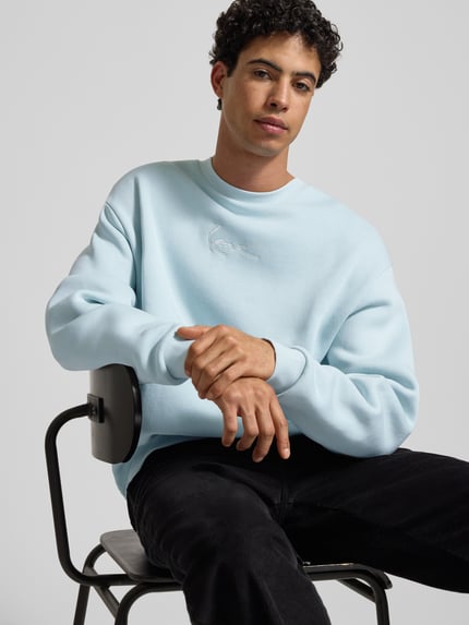 Męski model nosi Sweatshirt mit Label-Stitching od KARL KANI, niebieski, bawełniany miks, luźny krój, widok całej sylwetki z przodu.