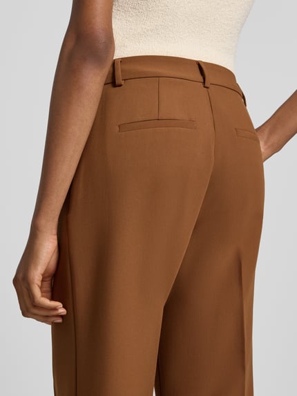 Frauenmodel trägt Straight Fit Hose mit Viskose-Anteil von Rich & Royal in Braun, glatte Textur, Gesäßtaschen, Detailaufnahme Rückansicht. Damen Hose, elastischer Viskose-Mix, Bügelfalten, Haken- und Reißverschluss, Bundweite 37 cm, Innenbeinlänge 70 cm.