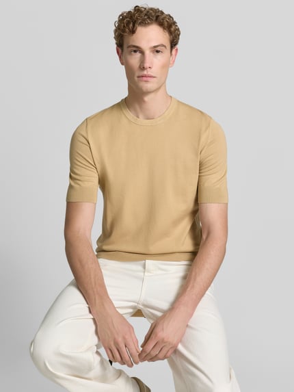 Męskimodel nosi Slim Fit T-Shirt aus Feinstrick Modell 'SAN CARL-CV' od HUGO, beżowy, gładka faktura, jasne spodnie, ujęcie z przodu, męski t-shirt