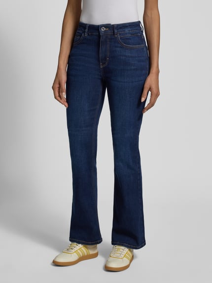 Modelka nosi Slim Fit Bootcut Jeans aus Baumwoll-Mix Modell 'STELLA' von Tom Tailor, denim, krój slim fit, wysokie szwy, mieszanka bawełny, 5 kieszeni, kontrastowe szwy, naszywka z logo, nity, zapięcie na guzik i ukryty zamek błyskawiczny. Ganzkörperansicht von vorne.
