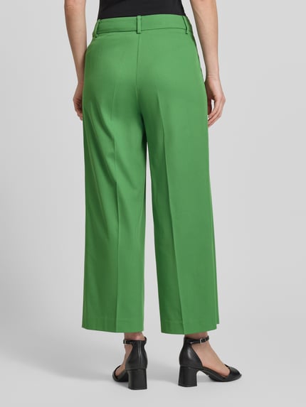 Frauenmodel trägt Wide Leg Hose aus Viskose-Mix mit Bügelfalten von More & More in Grün, Stoff leicht, Ganzkörperansicht Rückansicht. Damen Hose mit Baumwoll-Anteil, Knopf- und Reißverschluss, Bundweite 39 cm, Innenbeinlänge 66 cm.