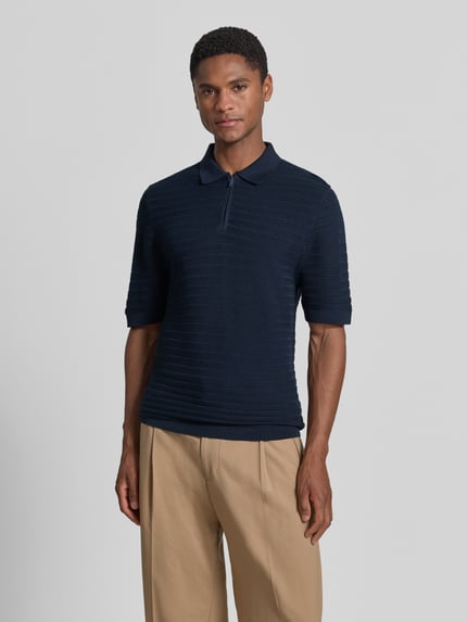 Męski model nosi Regular Fit Poloshirt mit kurzem Reißverschluss od MCNEAL, mieszanka bawełny i wiskozy, fakturowany wzór, kołnierzyk polo, krótki zamek błyskawiczny, długość tyłu w rozmiarze M: 69 cm, długość rękawów w rozmiarze M: 26 cm, granatowy, proste kształty, jednolita faktura, Ganzkörperansicht z przodu.