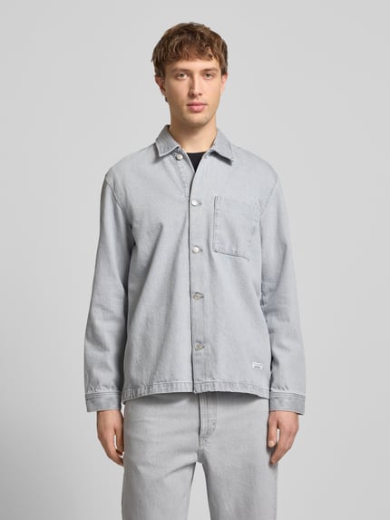 Männermodel trägt Regular Fit Hemdjacke aus reiner Baumwolle von Marc O'Polo Denim in Denim-Optik, Umlegekragen, Langarm, Brusttasche, einreihige Knopfleiste, Label-Patch, helle Farbgebung, glatte Textur, Ganzkörperansicht von vorne.