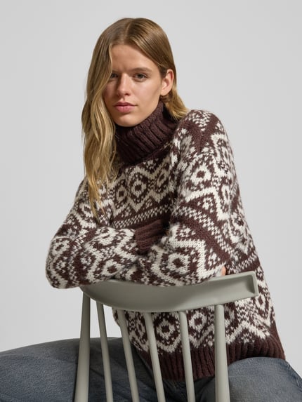 Vrouwenmodel draagt Regula Fit coltrui met all-over Noors motief van Only, grofgebreid, bruin en wit, detailopname bovenlichaam.
