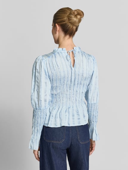 Frauenmodel trägt Bluse in tailliertem Schnitt mit Smok-Details Modell 'RAVA' von YAS, hellblau mit feiner Struktur, Ganzkörperansicht Rückansicht. Viskose-Mix mit Lyocell-Anteil, Rückenlänge 54 cm, Ärmellänge 65 cm.