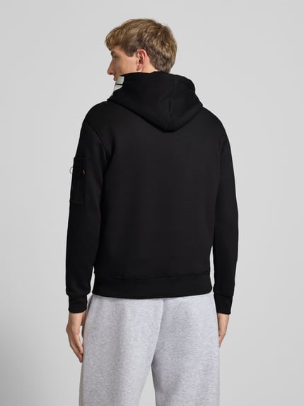 Männermodel trägt Regular Fit Hoodie aus Baumwoll-Mix mit Label-Patch von Alpha Industries, Schwarz, Ärmel-Tasche, Rückenansicht.