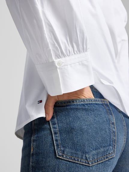 Männermodel trägt Regular Fit Langarmbluse aus reiner Baumwolle von Tommy Hilfiger, biała, logo, detal na rękawie, zbliżenie na dolną część koszuli.