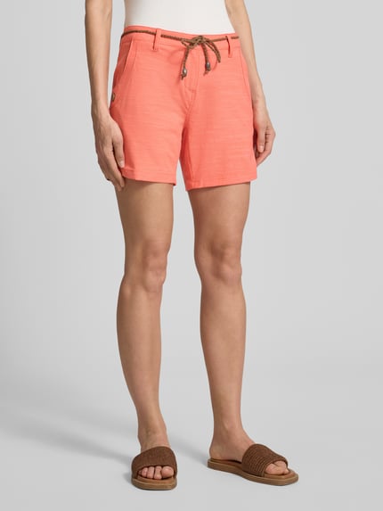 Frauenmodel trägt Bermudas mit Bindegürtel und Eingrifftaschen von G.I.G.A. DX aus Baumwoll-Mix mit Stretch-Anteil, Straight Fit, Knopf- und Reißverschluss, sichtbare Struktur in Koralle, Seitentaschen mit Knopfverschluss, Ganzkörperansicht von vorne.