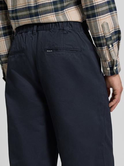 Männermodel trägt Bundfaltenhose mit Twillstruktur von Barbour, unifarben, Gesäßtaschen, Detailaufnahme Rückansicht.