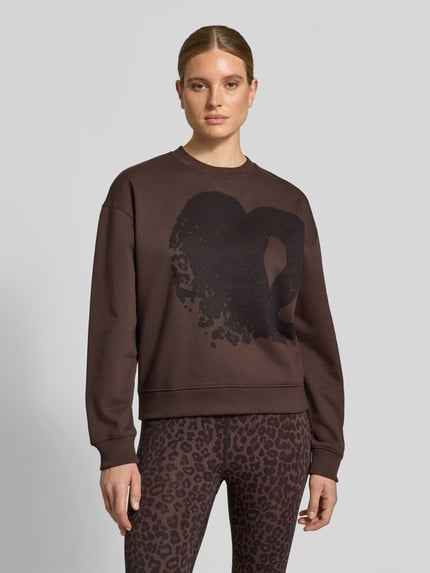 Frauenmodel trägt Oversized Sweatshirt aus Baumwolle von Lala Berlin, braun mit schwarzem Motiv-Print, gerippte Abschlüsse, Ganzkörperansicht von vorne.