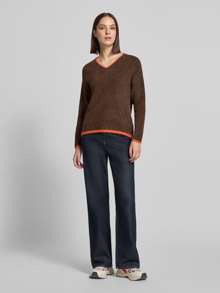 Kobieta nosi sweter z dzianiny z dekoltem w serek, paski w kontrastowym kolorze, model 'Ro44sie' od ZABAIONE, krój regular fit, długość tyłu 62 cm, długość rękawów 51 cm, zdjęcie całej sylwetki od przodu.