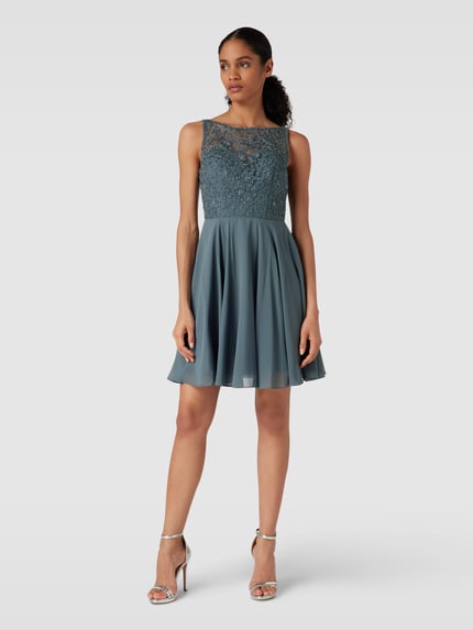 Frauenmodel trägt Regular fit Minikleid mit floralem Spitzenbesatz von Laona in semitransparenter Optik und Ziersteinbesatz, ärmellos, blickdichter Unterrock, Ganzkörperansicht von vorne.