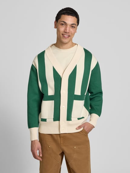 Männermodel trägt Cardigan mit Streifenmuster und V-Ausschnitt von BLKVIS in Grün und Creme, Reine Baumwolle, Relaxed-Fit, Ganzkörperansicht von vorne.