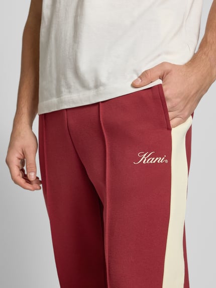 Männermodel trägt Sweatpants mit Längsnähten und elastischem Bund von KARL KANI, Baumwoll-Mix mit Stretch-Anteil, Label-Print, Nahaufnahme Oberkörper.