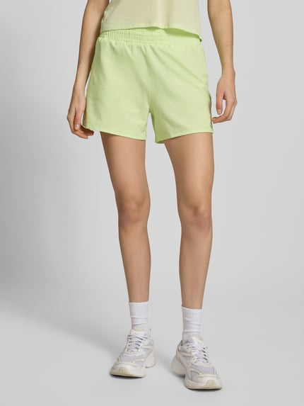 Kobiecy model nosi zielone szorty Regular Fit Shorts mit elastischem Bund Modell 'Kout' od Salomon, krój regular fit, z elastycznym pasem, zintegrowanymi figami, szerokość w rozmiarze S: 36 cm, długość wewnętrzna nogawki w rozmiarze S: 10 cm, widok całej sylwetki od przodu.