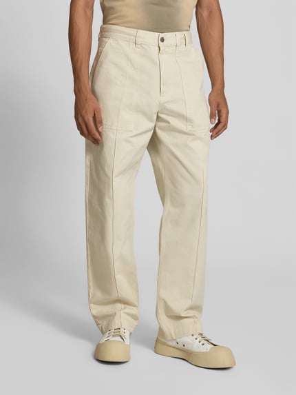 Männermodel trägt Straight Fit Hose aus reiner Baumwolle von Forét in Beige mit Eingrifftaschen, Gesäßtaschen, Knopf- und Reißverschluss, Ganzkörperansicht von vorne.