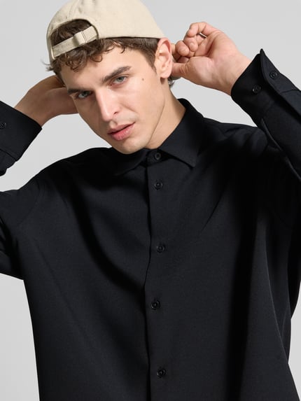 Männermodel trägt Oversized Hemdjacke mit Kentkragen Modell 'STUDIO' von SEIDENSTICKER STUDIO in Schwarz, Regular Fit, Nahaufnahme Oberkörper. Elastischer Material-Mix, durchgehende Knopfleiste, langärmlig, Rückenlänge bei Größe M 75 cm.