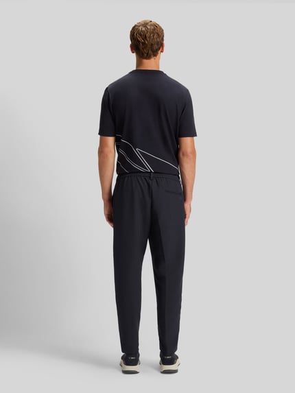Männermodel trägt Tapered Bundfaltenhose mit halbelastischer Bund Modell 'CONVERT-PLEAT' von BOSS Green, unifarben, Ganzkörperansicht Rückansicht.