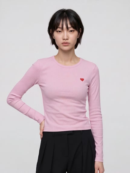 Frauenmodel trägt T-Shirt mit Herzstickerei von VERO MODA in Rosa, Slim Fit, Feinripp, Rundhals, lange Ärmel, Ganzkörperansicht von vorne.