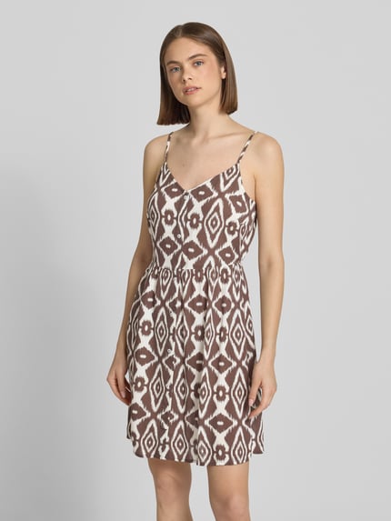 Frauenmodel trägt Leicht ausgestelltes Minikleid aus reiner Viskose Modell 'TALA' von Pieces mit braun-weißem Allover-Muster, V-Ausschnitt, verstellbaren Spaghettiträgern und geradem Saum, floral gemustert, Ganzkörperansicht von vorne.