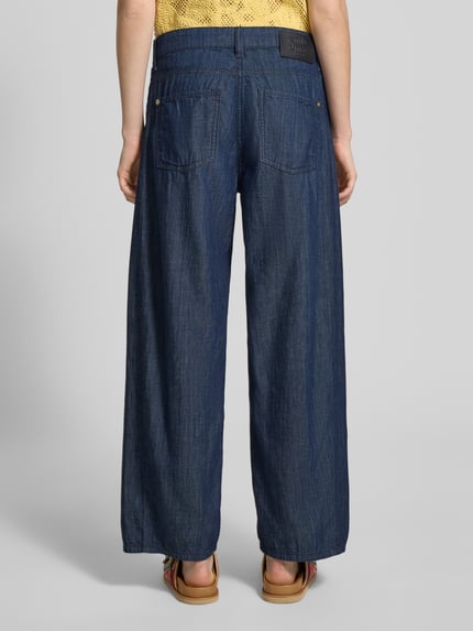 Frauenmodel trägt Barrel Fit Jeans aus reiner Baumwolle Modell 'ORIA' von Cambio in Denim-Optik mit Twill-Materialverarbeitung, 5-Pocket-Design, Label-Patch, Gürtelschlaufen und Knopf-Verschluss, Ganzkörperansicht Rückansicht.