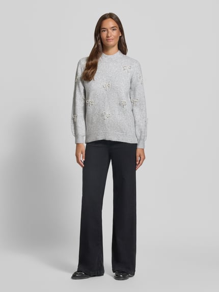 Frauenmodel trägt Strickpullover mit Stehkragen und Perlen von Apricot, hellgrau, Regular Fit, Perlenapplikation, schwarze Hose, Ganzkörperansicht von vorne.