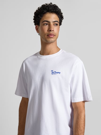 Männermodel trägt Relaxed Fit T-Shirt aus reiner Baumwolle Modell 'MILO' von Only & Sons, jednokolorowy, krój relaxed fit, nadruk z napisem oraz motywem, okrągły dekolt, krótki rękaw, materiał: bawełna, Nahaufnahme górnej części ciała.