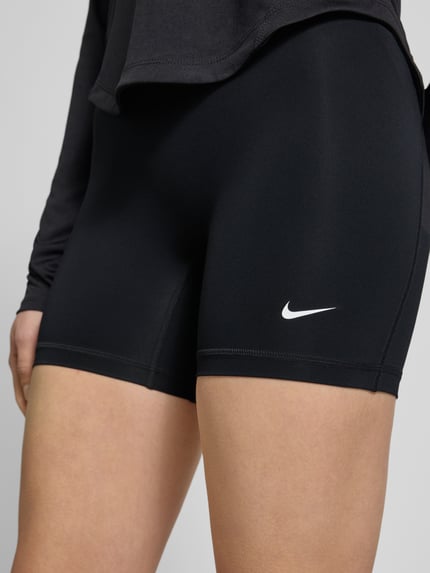 Frauenmodel trägt Radlerhose mit elastischem Bund und Logo von NIKE TRAINING, schwarz, körpernaher Schnitt, Logo vorn, Nahaufnahme Oberkörper.