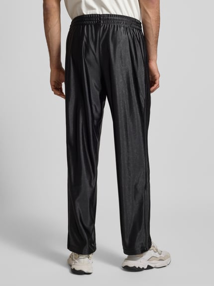Männermodel trägt Trainingshose mit Logo Modell 'FIREBIRD' von adidas Originals in Schwarz mit elastischem Bund, Regular Fit, Ganzkörperansicht Rückansicht.