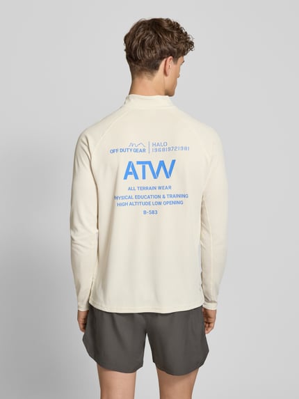Mężczyznamodel nosi Longsleeve mit Stehkragen und Reißverschluss Modell 'SORONA' von HALO, kremowy kolor, nadruk z tyłu, krój regular fit, długość tyłu w rozmiarze M: 70 cm, Ganzkörperansicht Rückansicht.