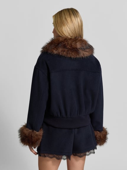 Frauenmodel trägt Wolljacke aus Woll-Viskose-Mix von Self-Portrait in Dunkelblau mit Kunstfellbesatz, Rückenansicht, Ganzkörperansicht Rückansicht. Regular Fit, Umlegekragen, Ärmelenden und Abdeckleiste sowie Eingrifftaschen, Rückenlänge 54 cm, Brustweite 57 cm, Ärmellänge 54 cm.