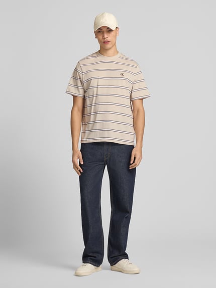 Männermodel trägt T-Shirt mit Logo-Stitching von Calvin Klein Jeans, reine Baumwolle, Gerader-Schnitt, Rundhalsausschnitt, Ganzkörperansicht von vorne.