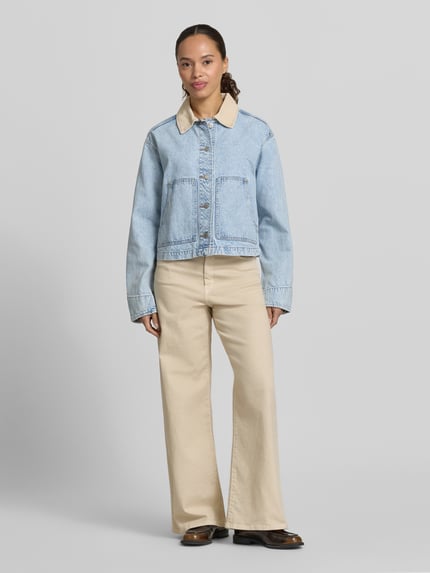 Vrouwenmodel draagt 'Cropped Jeansjacke mit Umlegekragen' van GAP in lichtblauw, puur katoen met knoopsluiting, steekzakken, platte kraag, oversneden schouders, afmetingen maat S: ruglengte 50 cm, schouderbreedte 50 cm, borstwijdte 55 cm, mouwlengte 60 cm, geheelbeeld vooraanzicht.