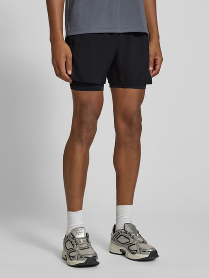 Mężczyzna nosi szorty im 2-in-1-Look mit Logo od ASICS, krój regular fit, efekt 2 w 1, logo, elastyczny pas, szerokość w rozmiarze M: 35 cm, widok całej sylwetki z przodu.