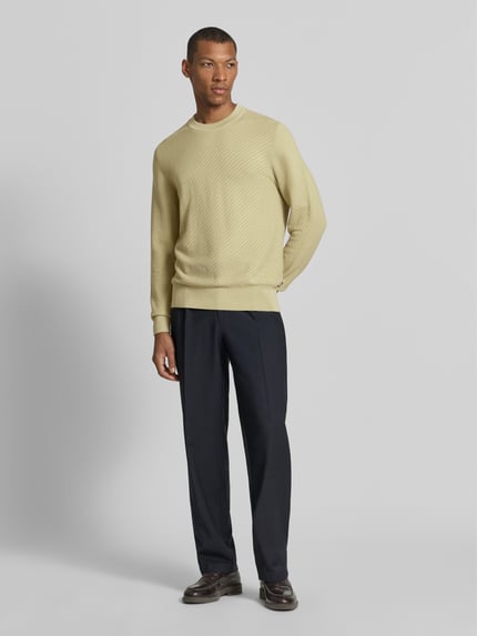 Männermodel trägt Regular Fit Pullover aus reiner Baumwolle Modell 'H-Lofranco' von BOSS in Gelb, schwarze Hose, Ganzkörperansicht von vorne, Herren Pullover von BOSS.