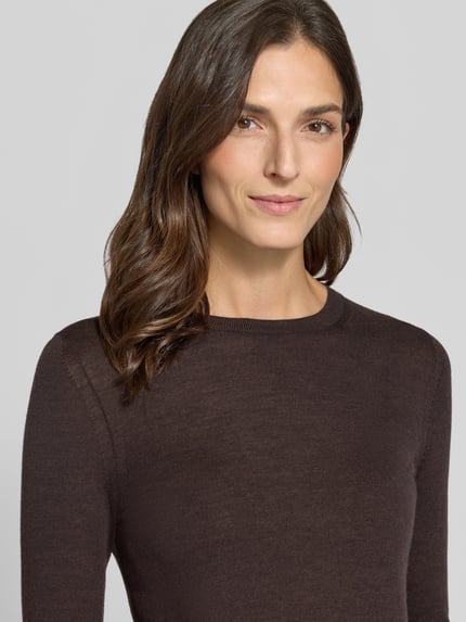 Frauenmodel trägt Pullover aus Wolle mit Feinstrickstruktur von BOSS in dunklem Braun, unifarben, Rundhals, Nahaufnahme Oberkörper.