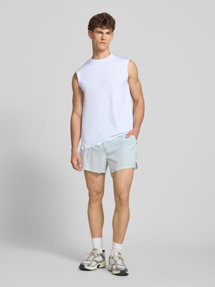 Männermodel trägt Relaxed Fit Top mit Logo-Print Modell 'OLIOS' von Ellesse, weiß, glatter Stoff, elastischer Material-Mix, Ganzkörperansicht von vorne.