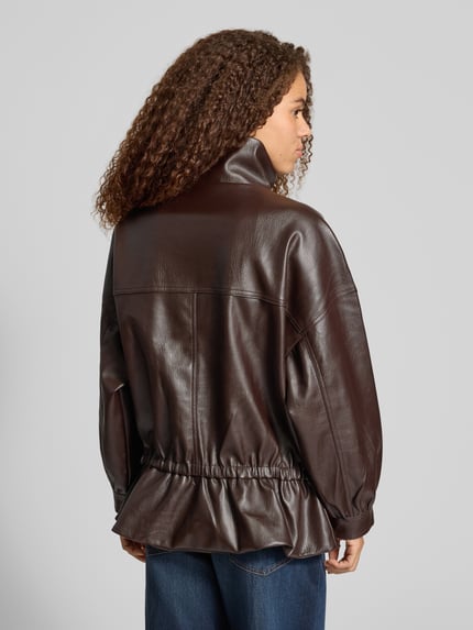 Vrouwenmodel draagt Jacke mit Stehkragen und Pattentaschen van Gina Tricot in donkere Leerlook met klepzakken en opstaande kraag, Getailleerd model, ruglengte maat S 70 cm, schouderbreedte 70 cm, borstwijdte 60 cm, mouwlengte 46 cm, Ganzkörperaanzicht achteraan.