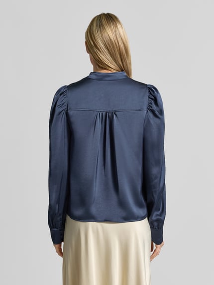 Vrouwenmodel draagt donkerblauwe Langarmbluse mit Stretch-Anteil Modell 'Rosslyn' van Neo Noir met ballonmouwen, satijnen look, rugdetails, ganzlichaamszicht achteraan.