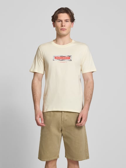 Männermodel trägt T-Shirt mit Logo und Rundhalsausschnitt von Jack & Jones in Beige, reine Baumwolle, Regular Fit, Ganzkörperansicht von vorne.