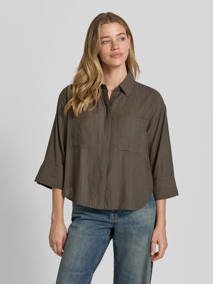 Modelka nosi Regular Fit Bluse aus Viskose-Mix mit 3/4-Arm Modell 'Forna' von OPUS, kolor khaki, widoczne kieszenie i kołnierzyk, krój regular fit, ukryta listwa guzikowa, długość tyłu 64 cm w rozmiarze 36, długość rękawa 40 cm w rozmiarze 36, widok całej sylwetki z przodu.