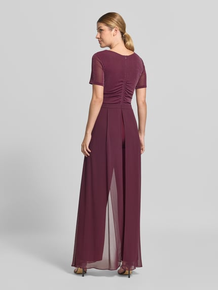 Vrouwenmodel draagt Regular Fit Jumpsuit uit mesh van Vera Mont in bordeauxrood, gladde stoffen en transparante details. Ganzlichaamsaanzicht achteraan.