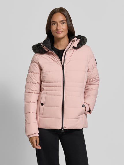 Frauenmodel trägt Jacke mit abnehmbarer Kapuze Modell 'ECLIPSE' von NAUTGÅRD in Hellrosa, sichtbarer Zweiwege-Reißverschluss, schwarze gestrickte Ärmelabschlüsse, seitliche Eingrifftaschen mit Druckknopfverschluss, Label-Patch am Ärmel, glatte und gesteppte Oberflächenstruktur, Ganzkörperansicht von vorne. Rückenlänge 65 cm, Schulterbreite 41 cm, Brustweite 51 cm, Ärmellänge 64 cm in Größe S.