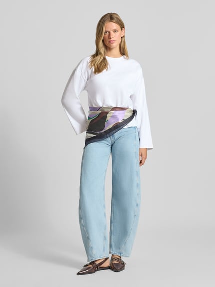 Frauenmodel trägt Oversized Langarmshirt aus reiner Baumwolle von REVIEW, weiße Farbe, lockerer Fit, Rundhalsausschnitt, Damen Langarmshirt mit überschnittenen Schultern und 58 cm Rückenlänge bei Größe S, kombiniert mit hellblauer Jeans, Ganzkörperansicht von vorne.