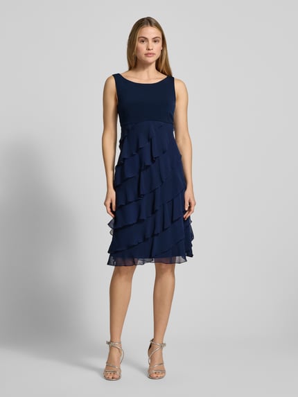 Frauenmodel trägt Knielanges Cocktailkleid mit Volants von Swing aus dunkelblauem Chiffon in A-Linie, Rundhalsausschnitt, Knielänge, Ganzkörperansicht von vorne. Rückenlänge 103 cm, Brustweite 31 cm bei Größe 36.