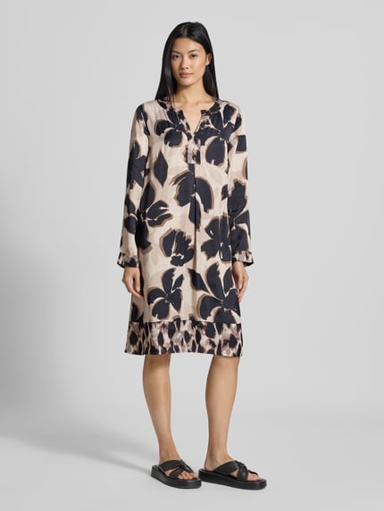 Frauenmodel trägt Figurumspielendes Freizeitkleid aus reiner Viskose Modell 'NOS JULI' von Betty Barclay mit beigem Grundton und großflächigem dunklen Blumenmuster, glatte Textur, Ganzkörperansicht von vorne, Damen Freizeitkleid von Betty Barclay.