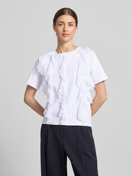 Modelka kobieca ma na sobie T-Shirt mit Rüschen und Rundhalsausschnitt od Christian Berg Woman, biała bawełna, prosty krój, przód pełny kadr.
