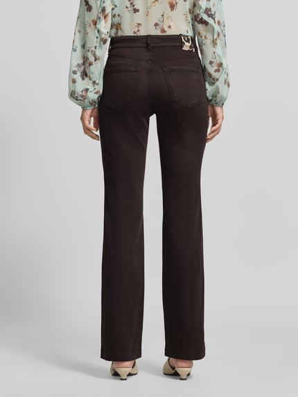 Kobiece model prezentuje Flared Fit Jeans mit Lyocell-Anteil od Marc Cain, elastyczna mieszanka materiałów, 5 kieszeni, zapięcie na guzik i zamek błyskawiczny, szerokość w rozmiarze 36: 37 cm, długość wewnętrzna nogawki: 81 cm, widok całej sylwetki z tyłu.