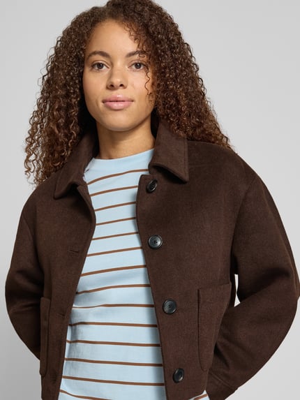 Frauenmodel trägt Bomberjacke mit Webpelzkragen Modell 'ONLELINOR' von ONLY in Dunkelbraun, einreihige Knopfleiste, aufgesetzte Seitentaschen, Umlegekragen, Zierknöpfe, Cropped-Länge, Nahaufnahme Oberkörper.